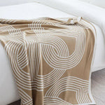 Vendbar strikket plaid med geometrisk labyrintmønster over sofa