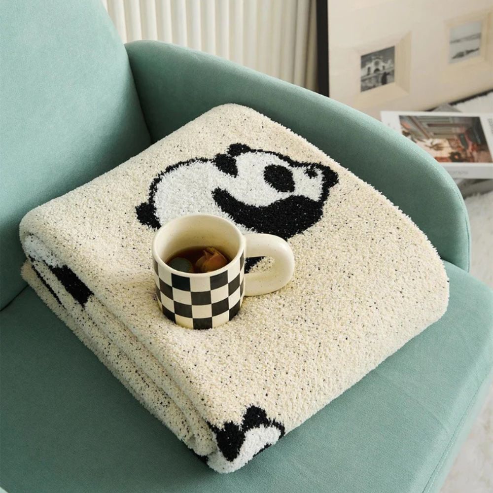 Strikket tæppe med yndigt pandamotiv over sofa