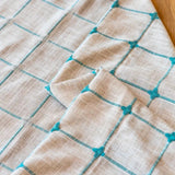 Boho gardin med turkis broderi og kvaster foran et vindue