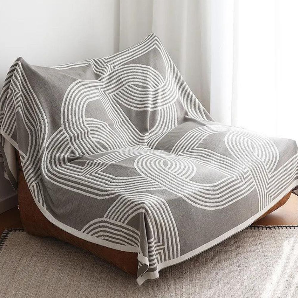 Vendbar strikket plaid med geometrisk labyrintmønster over sofa