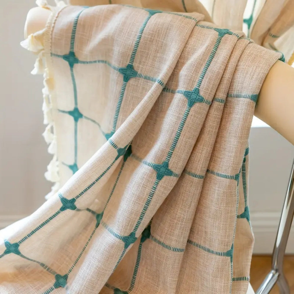Boho gardin med turkis broderi og kvaster foran et vindue