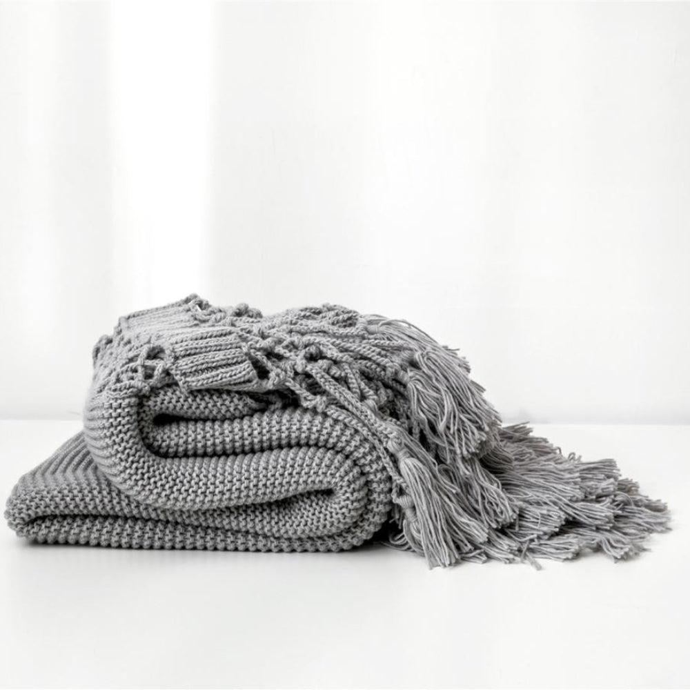 Strikket plaid med kvaster draperet over sofa