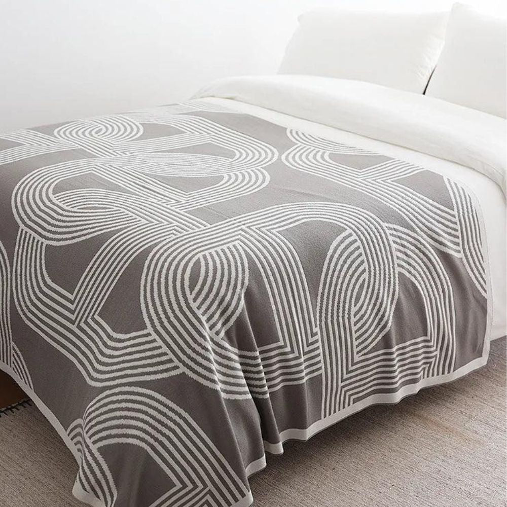 Vendbar strikket plaid med geometrisk labyrintmønster over sofa