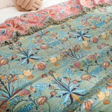 Vendbart bomuldstæppe med blomsterjacquard og kvaster på seng