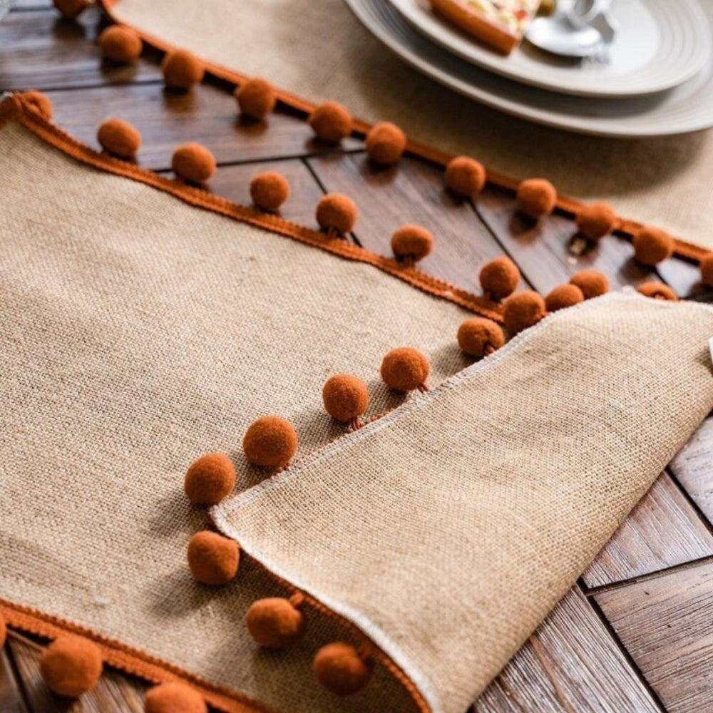 Bordløber i jute med orange pomponer på spisebord
