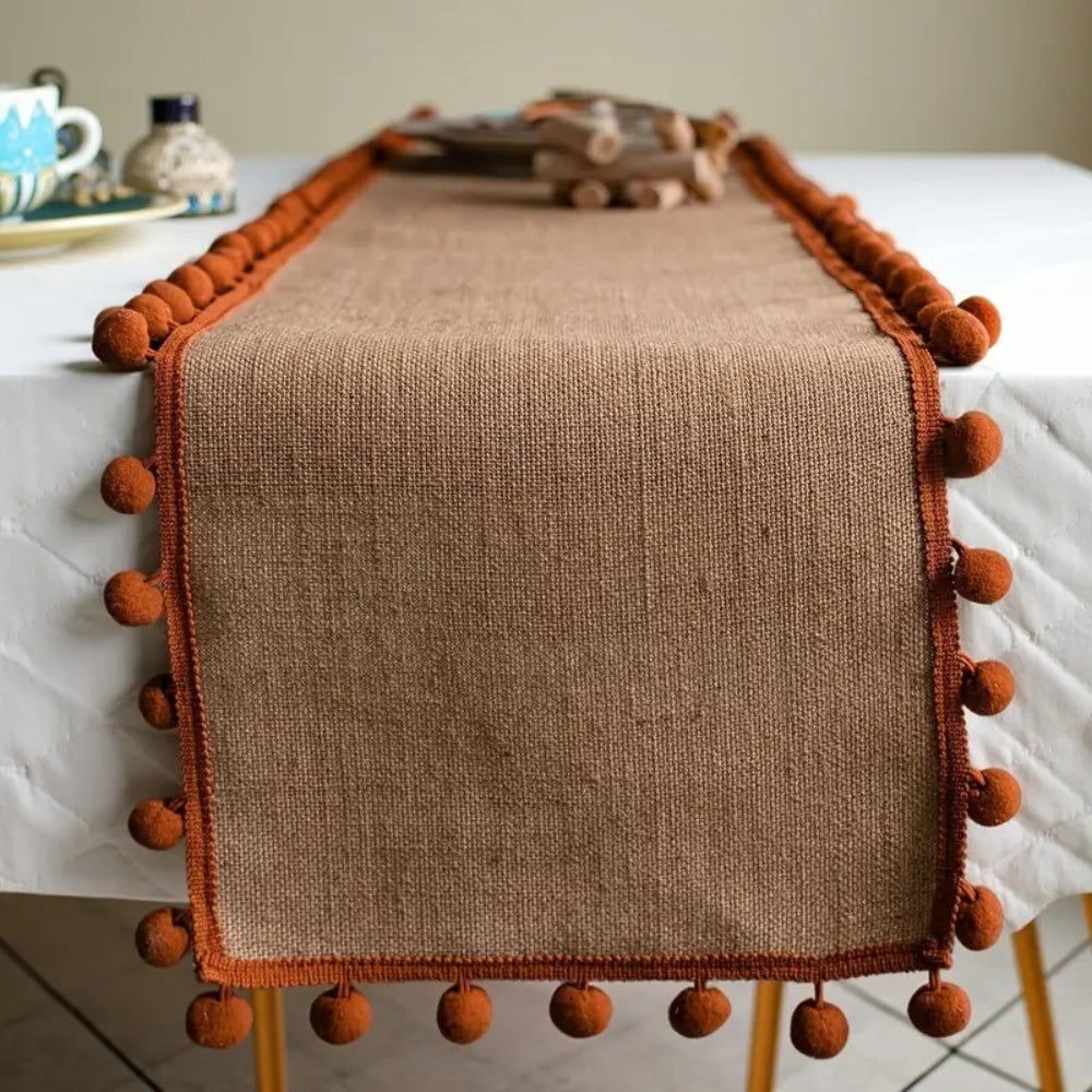 Bordløber i jute med orange pomponer på spisebord