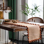 Bordløber i jute med orange pomponer på spisebord