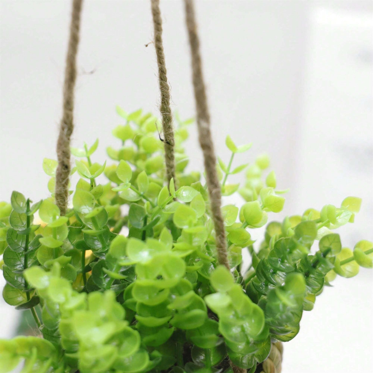 Hængende kunstig plante i vævet kurvepotte på altan