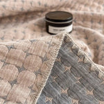 Vendbart bomuldstæppe i matelassé med geometrisk mønster over sofa