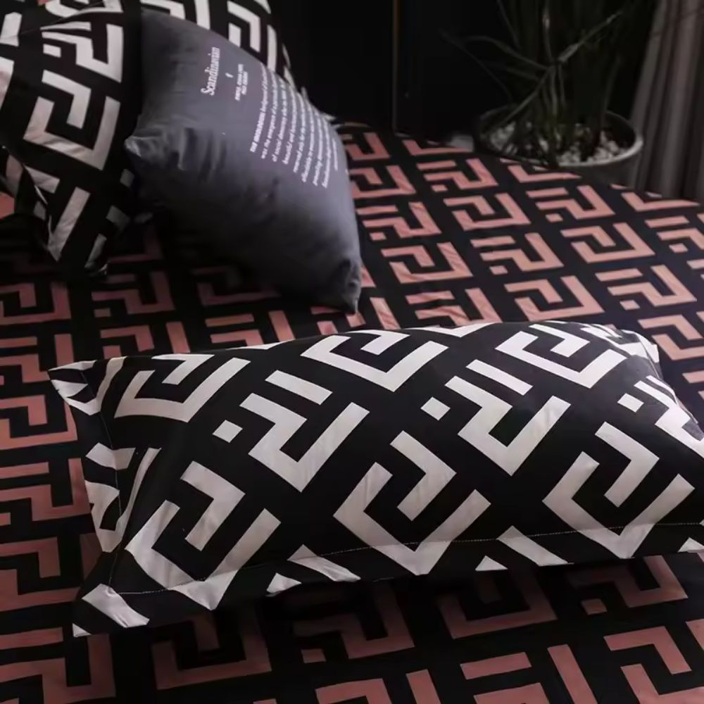 Sengetøjssæt med sort geometrisk labyrintmønster på en redt seng