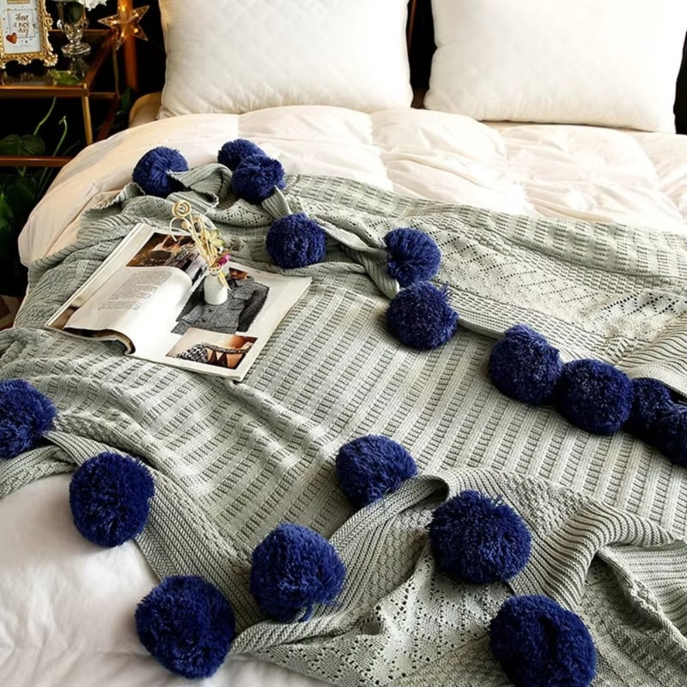 Strikket plaid med bløde pomponer i macaronfarver på sofa