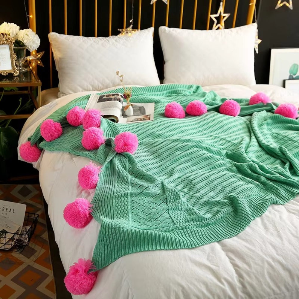 Strikket plaid med bløde pomponer i macaronfarver på sofa
