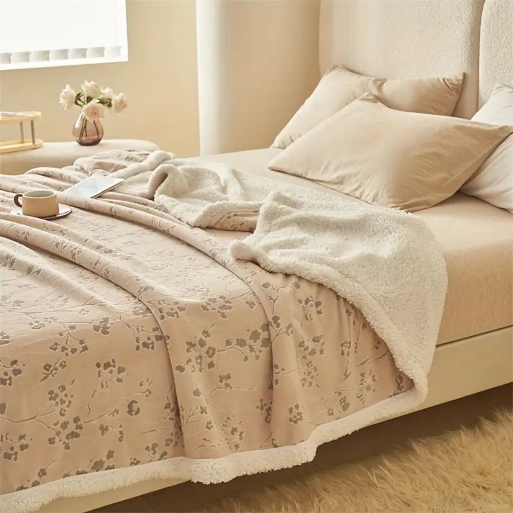 Plysset beige fleecetæppe med blomstermønster over en sofa